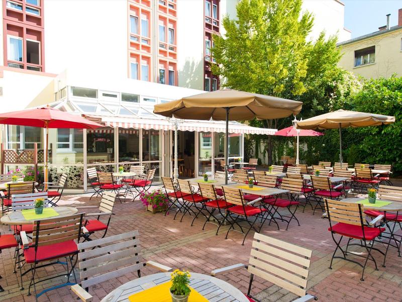 Un área al aire libre soleada de una cafetería con sillas coloridas y grandes sombrillas.