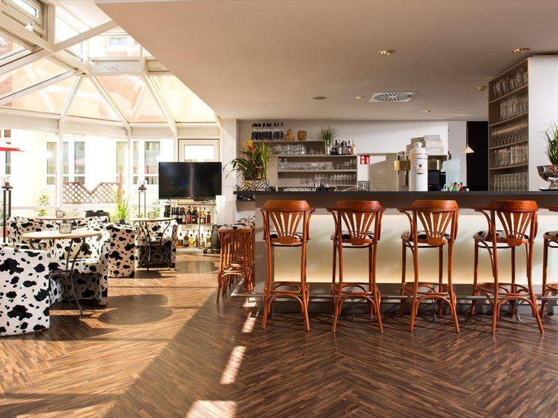 Área de bar de hotel luminosa con suelo de madera, taburetes altos y muebles con estampado de vaca a la luz del día.