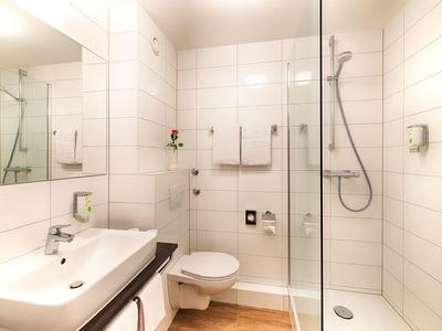 Helles Badezimmer mit Waschbecken, Toilette und begehbarer Dusche mit Glaswand.