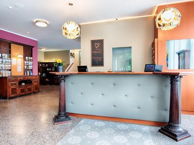 Heller Empfangsbereich mit elegantem Tresen, Deckenlampen und bunten Wänden in warmen Tönen.