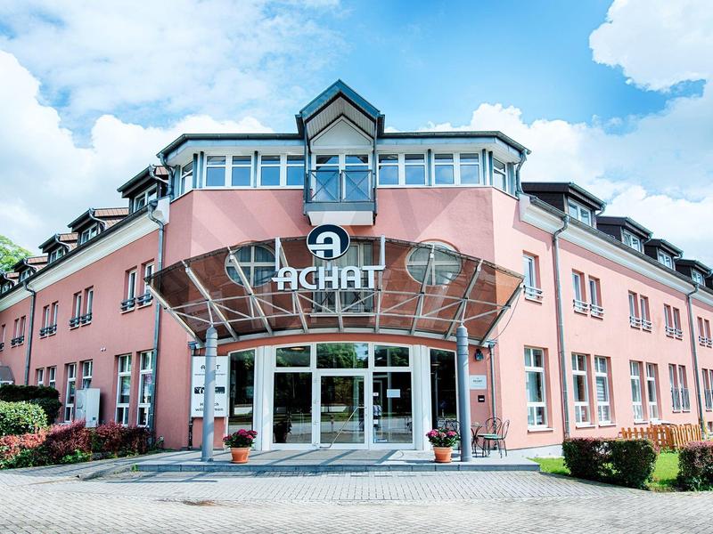 Modernes, rosafarbenes Gebäude mit Glasvordach und großen Fenstern unter blauem Himmel.