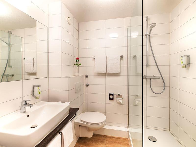 Helles Badezimmer mit weiß gekachelten Wänden, Waschbecken, Toilette und begehbarer Dusche.