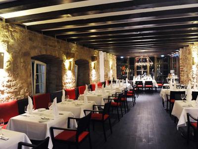 Stilvolles Restaurant mit weißen Tischtüchern, roten Stühlen und Steinwänden in gemütlicher Atmosphäre.