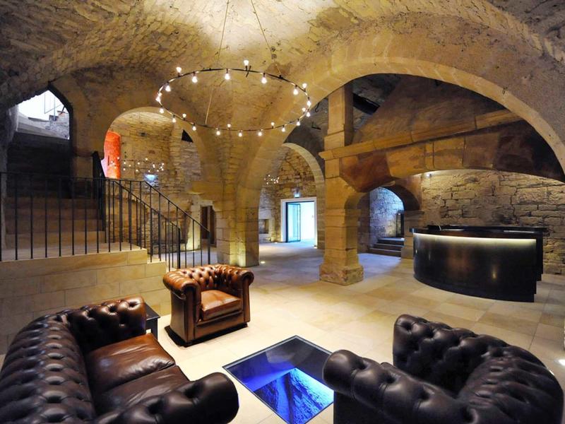 Historischer Gewölbekeller mit rauen Steinwänden, Rundbögen und modernen Ledersesseln in dunklem Braun.