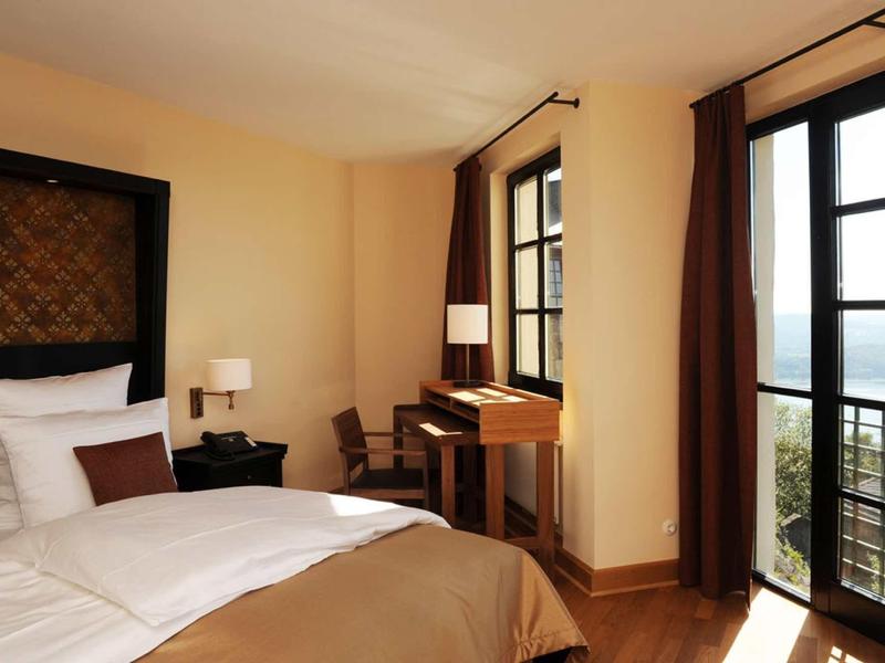 Gemütliches Schlafzimmer mit großem Bett, Holzboden, Schreibtisch und Balkon mit Meerblick.