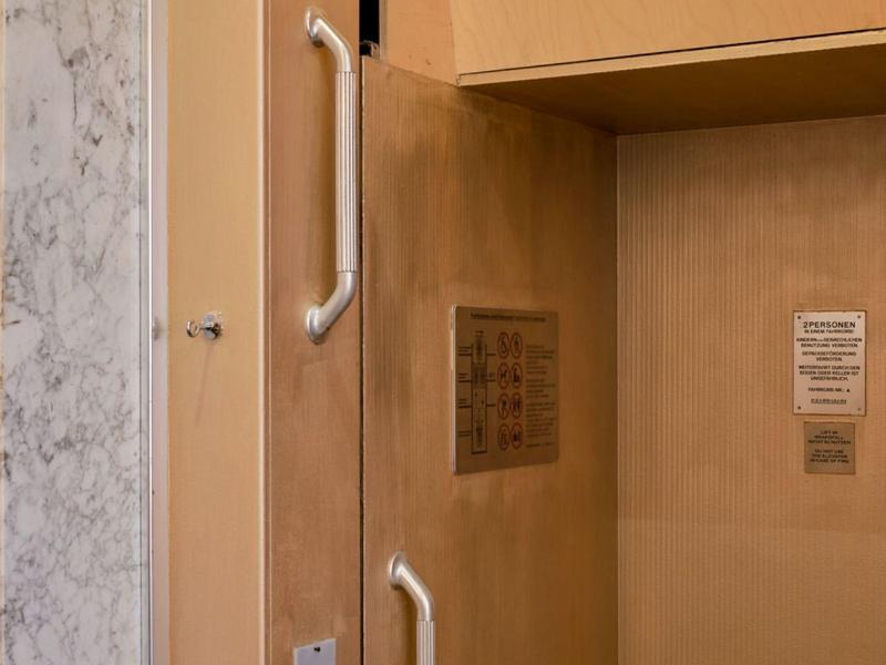 Vue intérieure d'un ascenseur avec des murs marron clair et des poignées métalliques