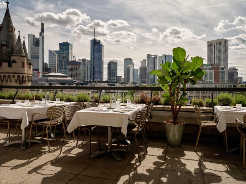 Terrasse sur le toit avec tables dressées, chaises et vue sur la skyline de la ville sous un ciel nuageux.