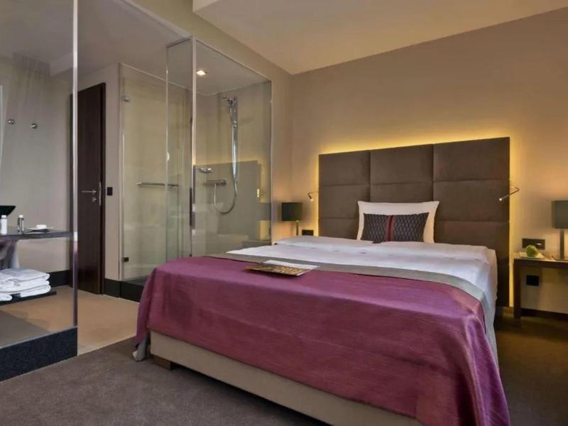 Chambre d'hôtel moderne avec lit double, douche en verre et éclairage chaleureux.