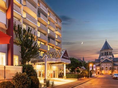 Hotel con ingresso illuminato e chiesa sullo sfondo al tramonto.