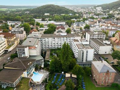 Complesso alberghiero con piscina, sdraio e ambiente boschivo in una città con colline sullo sfondo