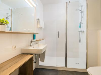 Modernes Bad mit Waschtisch, Spiegel, Dusche mit Glasabtrennung und Holzablage.