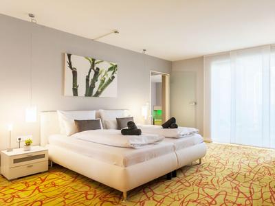 Modernes Hotelzimmer mit Doppelbett, Teppichboden und großem Fenster mit Vorhängen.