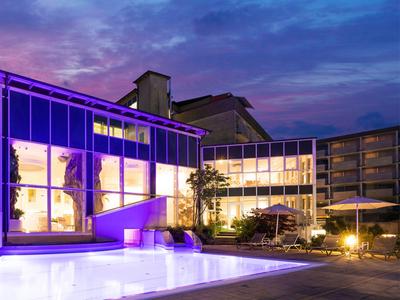 Modernes Hotelgebäude mit großzügigen Glasfronten bei Dämmerung, Außenbereich mit Sitzgelegenheiten und Beleuchtung.