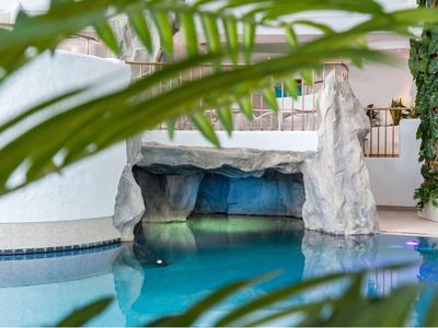 Piscina interna con grotta rocciosa e piante verdi in un hotel moderno.