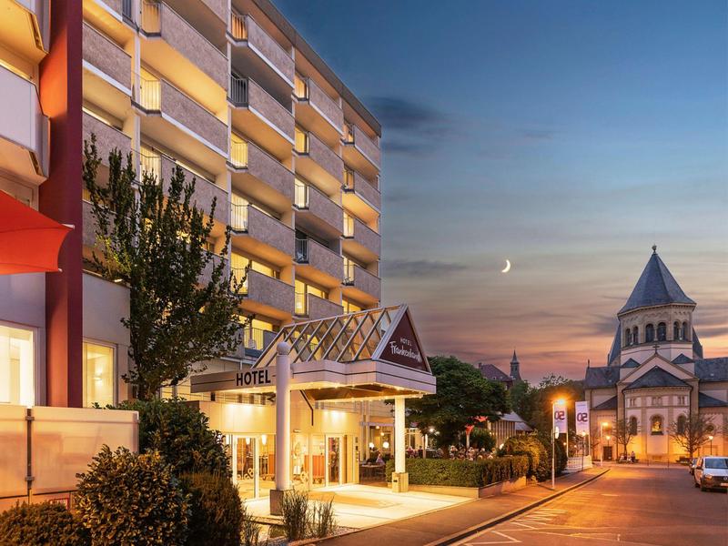 Hotel con ingresso illuminato e chiesa sullo sfondo al tramonto.