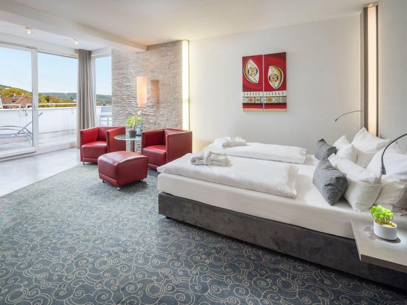 Camera d'hotel moderna con letto matrimoniale, zona salotto e ampia porta finestra sul balcone.