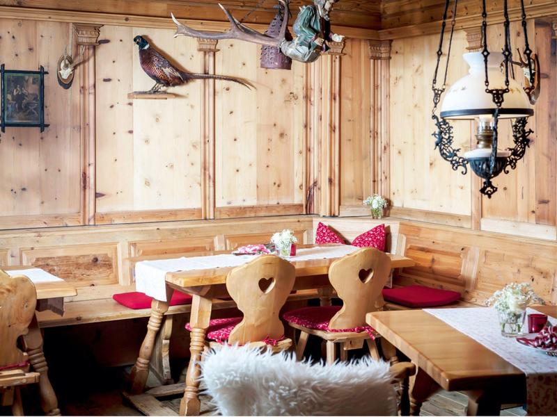 Accogliente panca ad angolo in legno con sedie a forma di cuore, cuscini rossi e decorazioni regionali in una locanda.