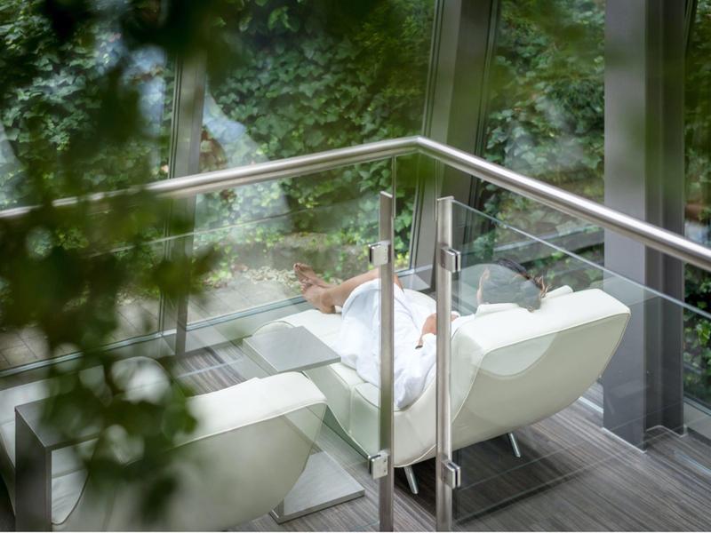 Persona rilassata in un'area salotto bianca moderna con pareti di vetro e vista sul verde esterno.