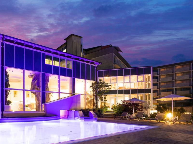 Edificio alberghiero moderno al crepuscolo con finestre illuminate e terrazza esterna.