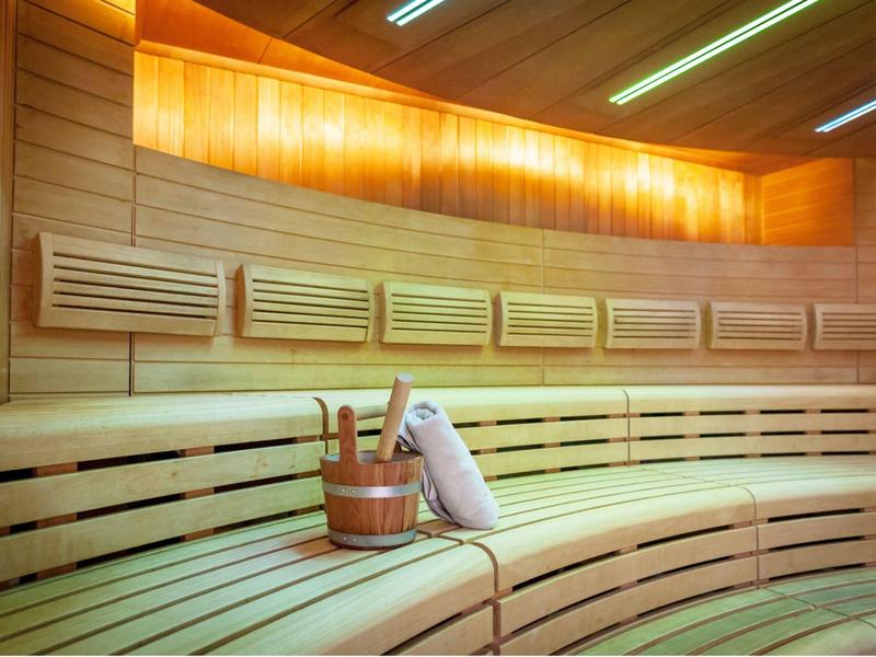 Sauna luminosa con panche di legno, secchio e mestolo dal design moderno.