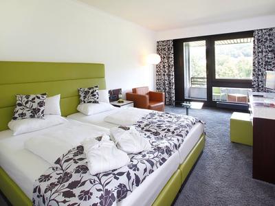 Nowoczesny pokój hotelowy z dwoma łóżkami, częścią wypoczynkową i balkonem z widokiem na zewnątrz.