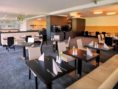 Nowoczesna część restauracyjna hotelu z stołami, krzesłami i elegancko złożonymi serwetkami.