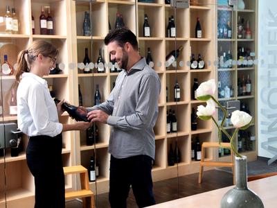 Ein Mann erhält Beratung zum Weinkauf in einem modernen Weinladen mit Holzwandregalen.