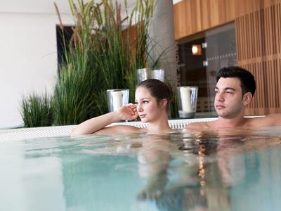 Para relaksuje się w hotelowym jacuzzi z nowoczesnym drewnianym wykończeniem w tle.