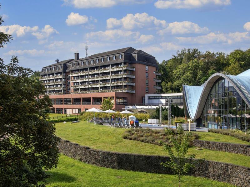 Nowoczesny budynek hotelu z przylegającą szklaną konstrukcją i ogrodem w słońcu