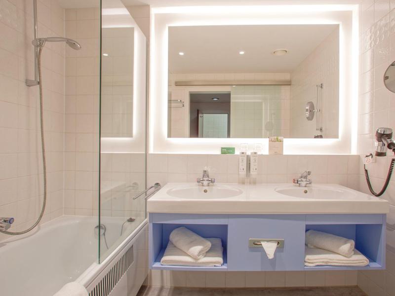 Jasna łazienka z wanną, podwójną umywalką, podświetlanym lustrem i suszarką do włosów.