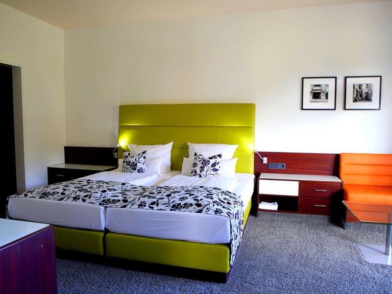 Nowoczesny pokój hotelowy z podwójnym łóżkiem, żółtym zagłówkiem i sofą w ciepłych kolorach