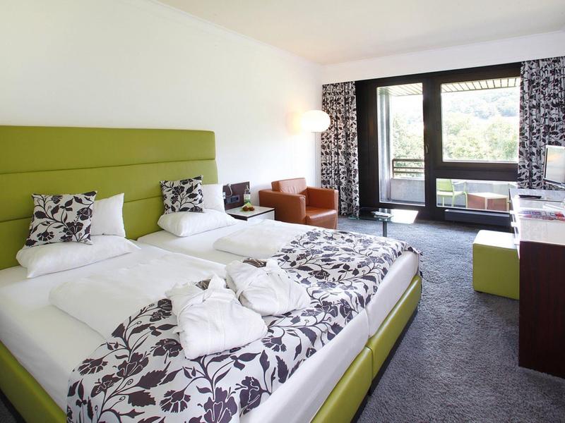 Nowoczesny pokój hotelowy z dwoma łóżkami, częścią wypoczynkową i balkonem z widokiem na zewnątrz.