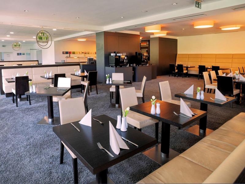 Nowoczesna część restauracyjna hotelu z stołami, krzesłami i elegancko złożonymi serwetkami.