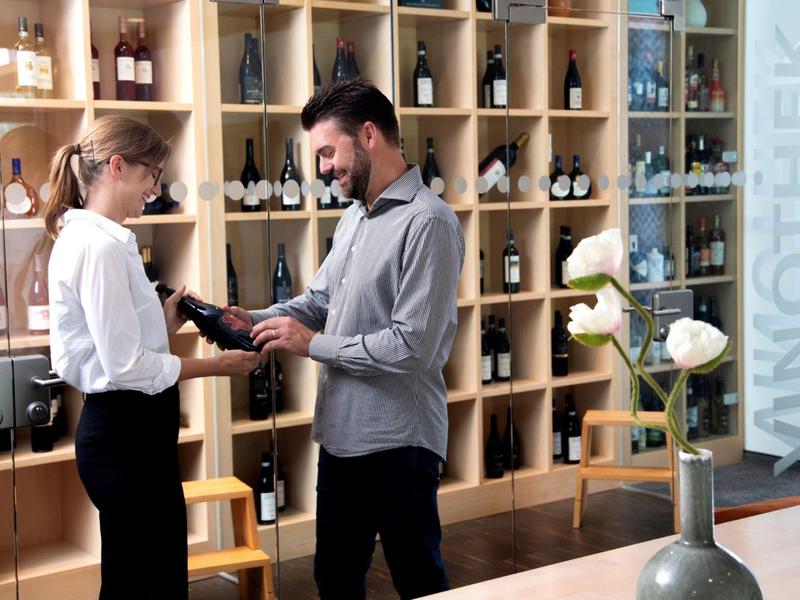 Mężczyzna otrzymuje porady dotyczące zakupu wina w nowoczesnym sklepie winiarskim z drewnianymi półkami.