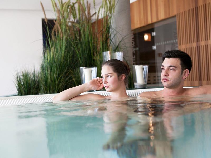 Para relaksuje się w hotelowym jacuzzi z nowoczesnym drewnianym wykończeniem w tle.