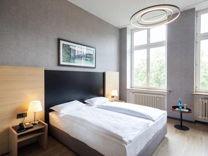 Habitación de hotel luminosa con cama doble, ventana grande e iluminación moderna.