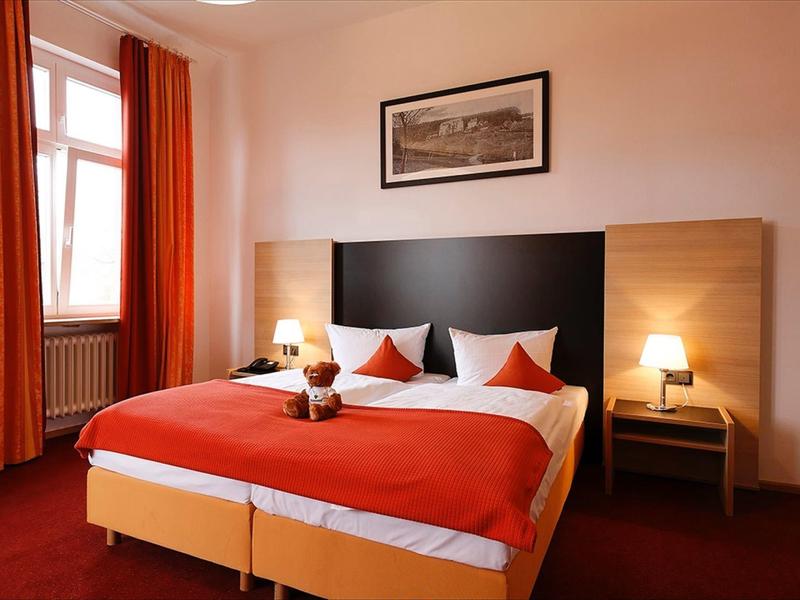 Acogedora habitación de hotel con cama doble, cortinas rojas y dos mesitas con lámparas.