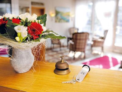 Eine Rezeption mit Blumenstrauß, Klingel und Zimmerschlüssel, unscharfer Wartebereich im Hintergrund.