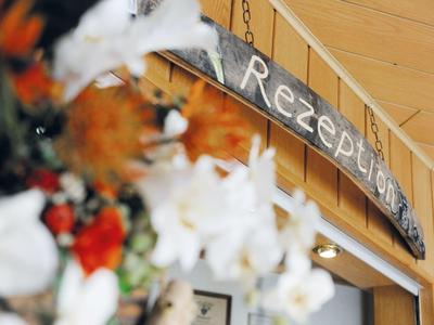 Verwittertes Holzschild mit der Aufschrift "Rezepte", umgeben von weißen und roten Blumen.