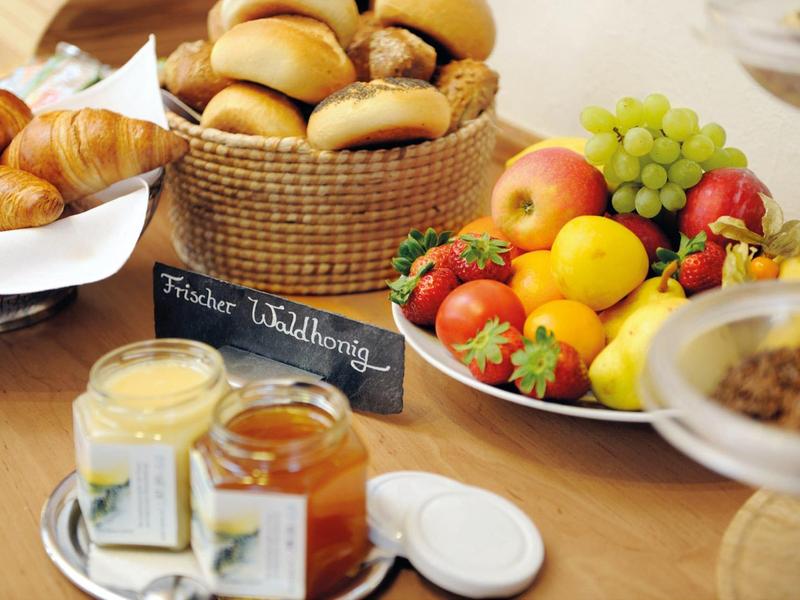 Frisches Frühstück mit Brötchen, Croissants, Früchten und verschiedenen Aufstrichen auf Holztisch.
