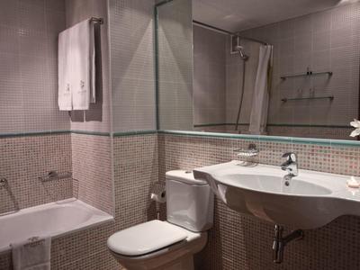 Kleines Badezimmer mit Badewanne, Toilette, Waschtisch und großen Spiegeln an den Wänden.