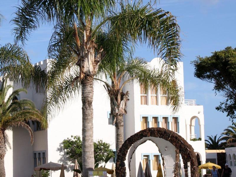 Hotelpool mit Palmen und weißem Gebäude im Hintergrund an einem sonnigen Tag.