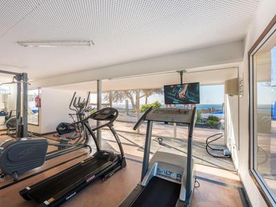 Moderner Fitnessraum mit Laufbändern und Fahrrädern, viel Tageslicht durch große Fenster.