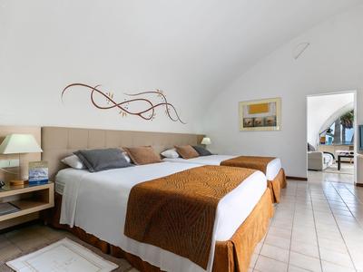 Helles Hotelzimmer mit zwei Einzelbetten, brauner Bettdecke, modernem Wanddekor und Blick in angrenzenden Raum.