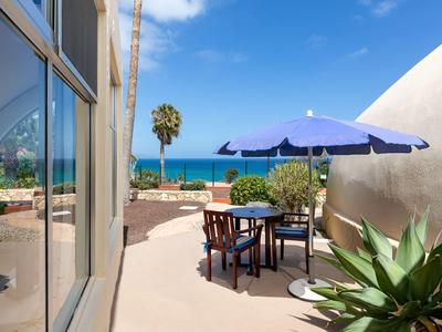 Terrasse mit Tisch, Stühlen und Sonnenschirm mit Blick auf das Meer und den blauen Himmel.