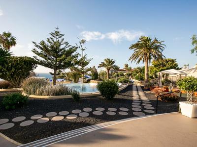 Außenbereich eines Hotels mit Pool, Palmen und Sitzgelegenheiten unter blauem Himmel.