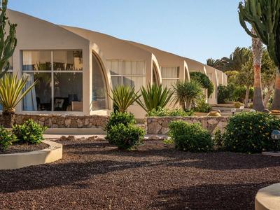 Moderne Hotelzimmer mit großen Fenstern und gepflegtem Garten mit Palmen und Sträuchern.