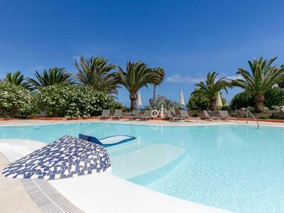Schwimmbad mit klarem Wasser, Sonnenschirm und Palmen im Hintergrund bei klarem Himmel.