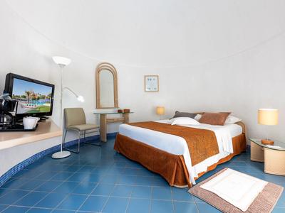 Modern eingerichtetes Hotelzimmer mit Doppelbett, blauen Fliesenboden und minimalistischem Design.