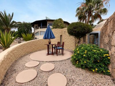 Gemütlicher Sitzbereich mit blauem Sonnenschirm und Pflanzen im Garten eines Hotels.